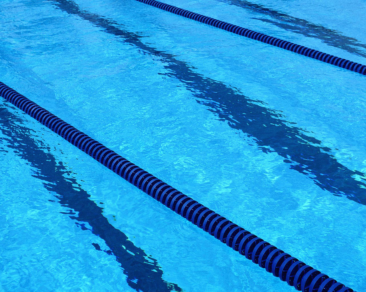 Close-up of bright blue swimming pool water with two diagonal lane dividers and rippling reflections.
